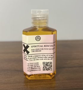 Small plastic bottle of yellow “Spiritual Rescue Oil” with a label that reads “Solution for food eaten in the dream,” placed on a wooden surface.