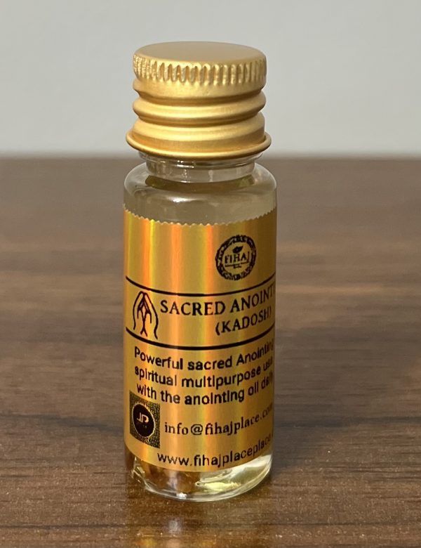 A small glass bottle of ‘Sacred Anointing Oil (Kadosh)’ with gold caps and holographic gold labels standing on a wooden surface. The labels display branding, usage instructions, and contact information.”