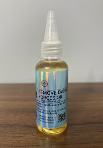“Bottle of Remove Dark Forces Oil with holographic label on a wooden surface, used for spiritual protection and cleansing.”