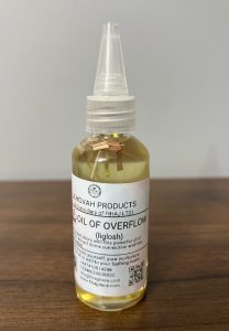 “Bottle of Jehovah Products Oil of Overflow (Iglosh) anointing oil with wooden herbs inside, placed on a wooden surface.”