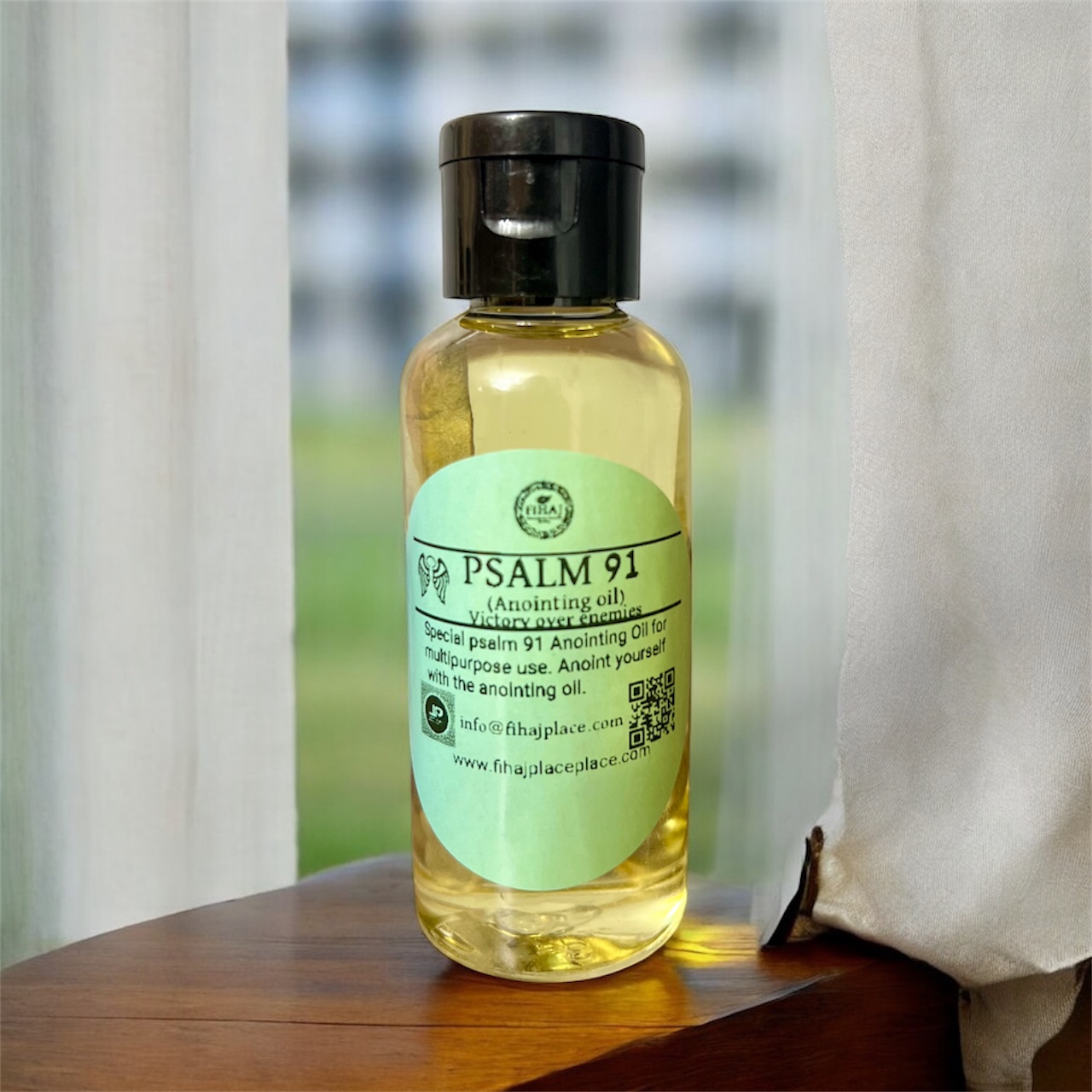 “Bottle of Psalm 91 anointing oil with green label on a wooden surface beside a white curtain.”