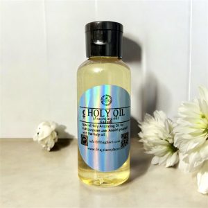 “Bottle of Holy Oil anointing oil on a light surface with white flowers in the background.”